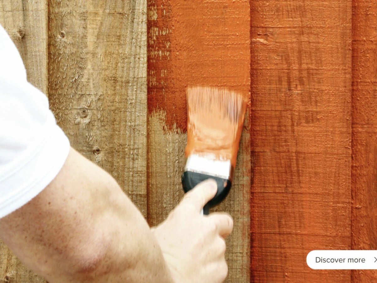fence-painting-hand-brushing-orange-surrey-decorators Close-up of brush applying orange fence stain to timber fence panel, Surrey Decorators