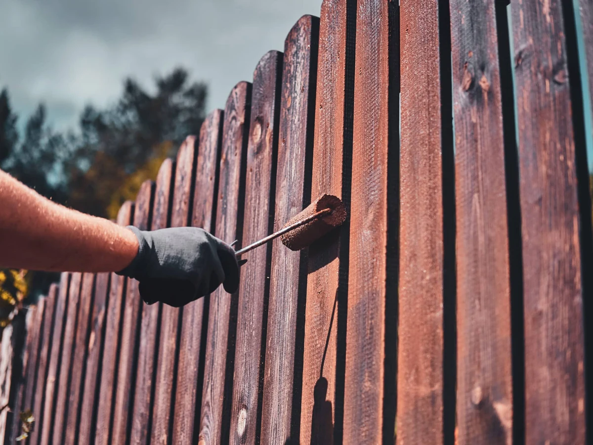 fence-painting-person-wooden-fence-surrey-decorators Fence painting in Surrey by Surrey Decorators, person applying stain to wooden garden fence