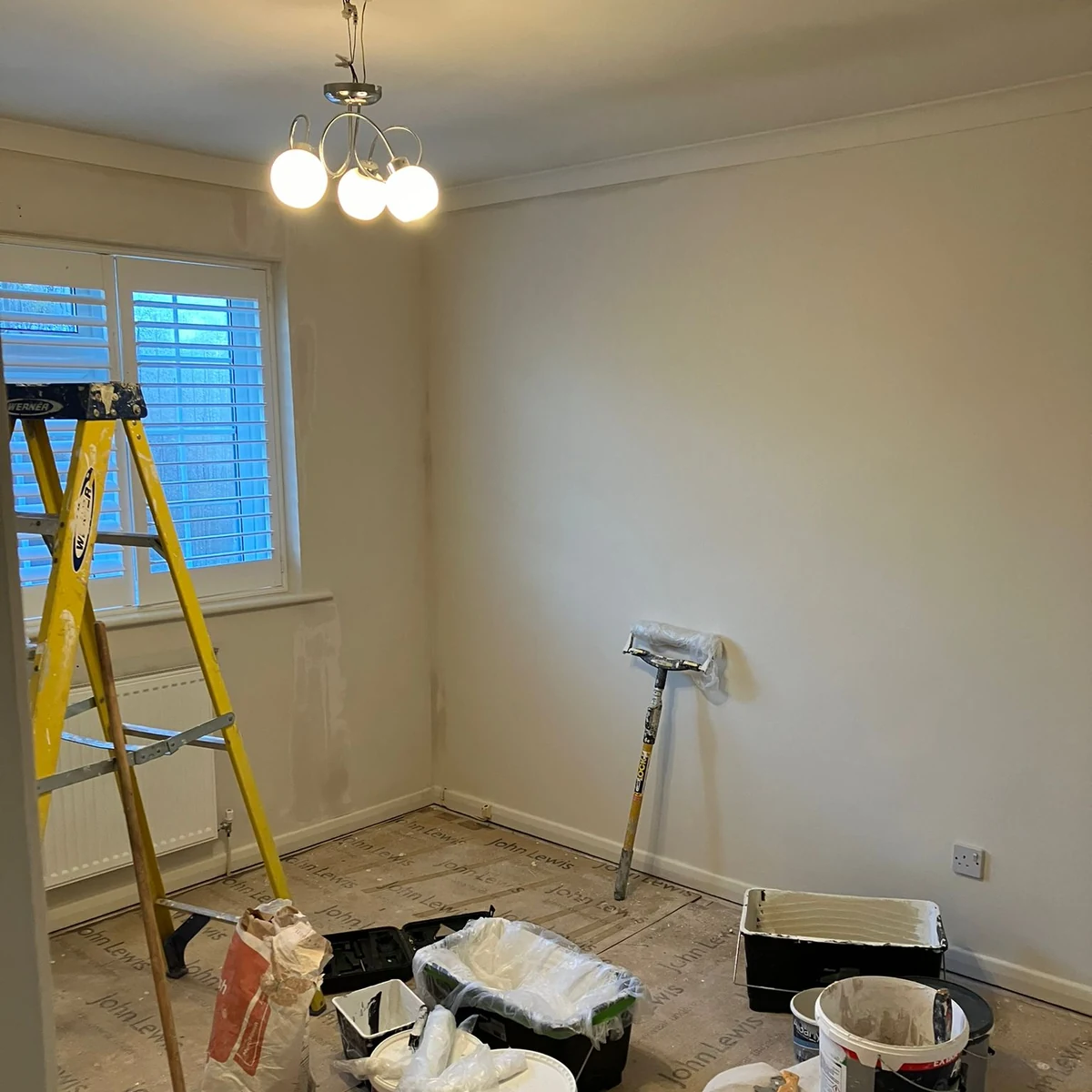 A room being decorated, with a stepladder, paint tins and a roller beside freshly painted walls